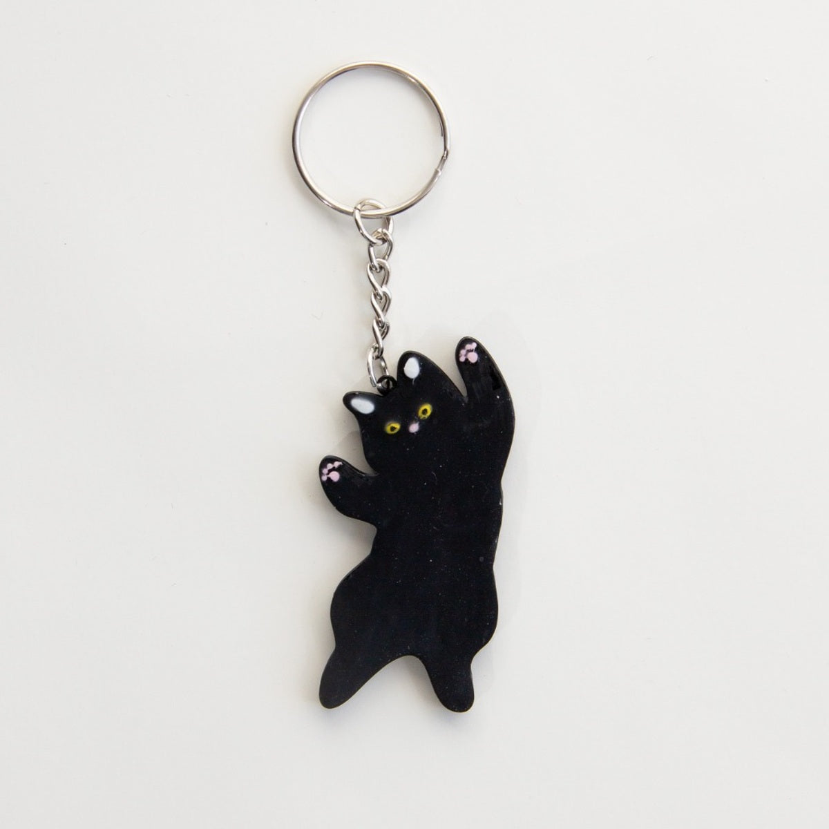 All-black stretching cat keyring with yellow eyes and pink paw details